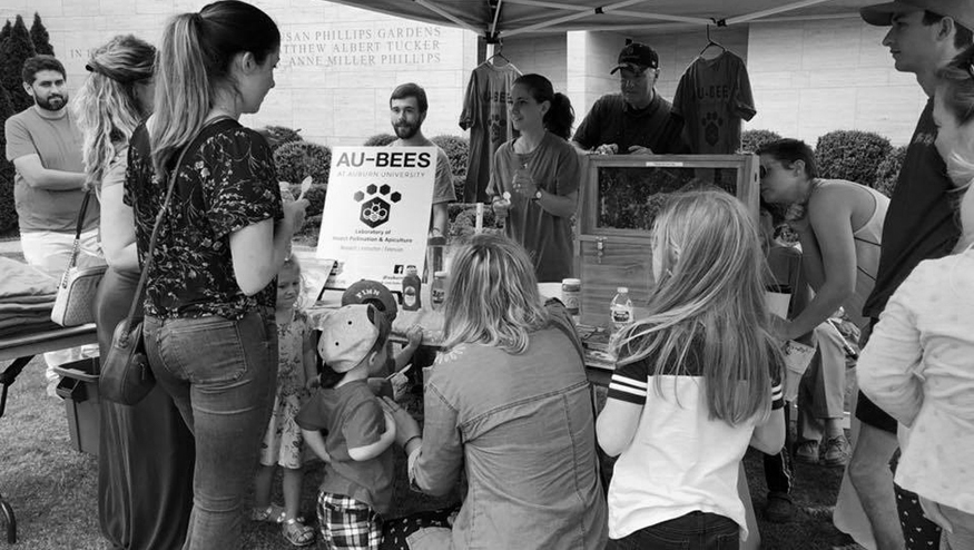 Auburn Bee Center employees talk to a group of children at an outdoor event underneath a tent